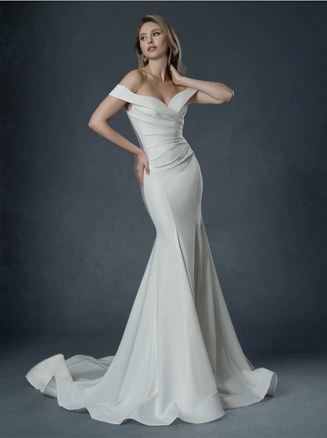 Model is wearing a minimalist off the shoulder wedding dress with a semi cathedral train
