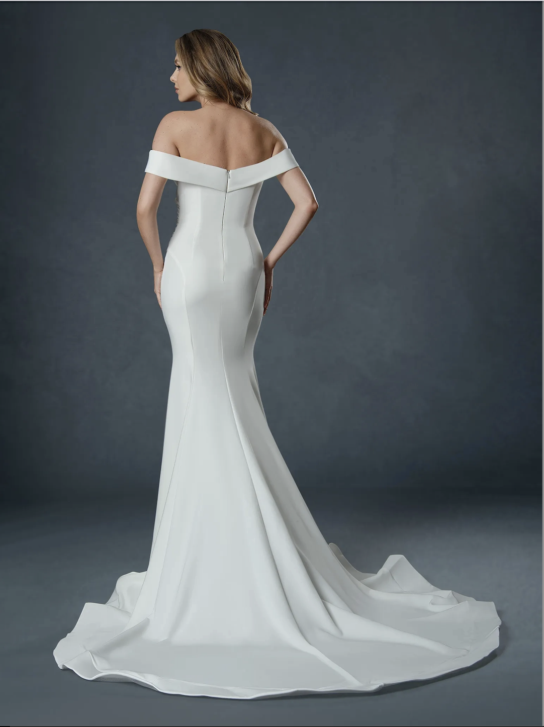 Model is wearing a minimalist off the shoulder wedding dress with a semi cathedral train